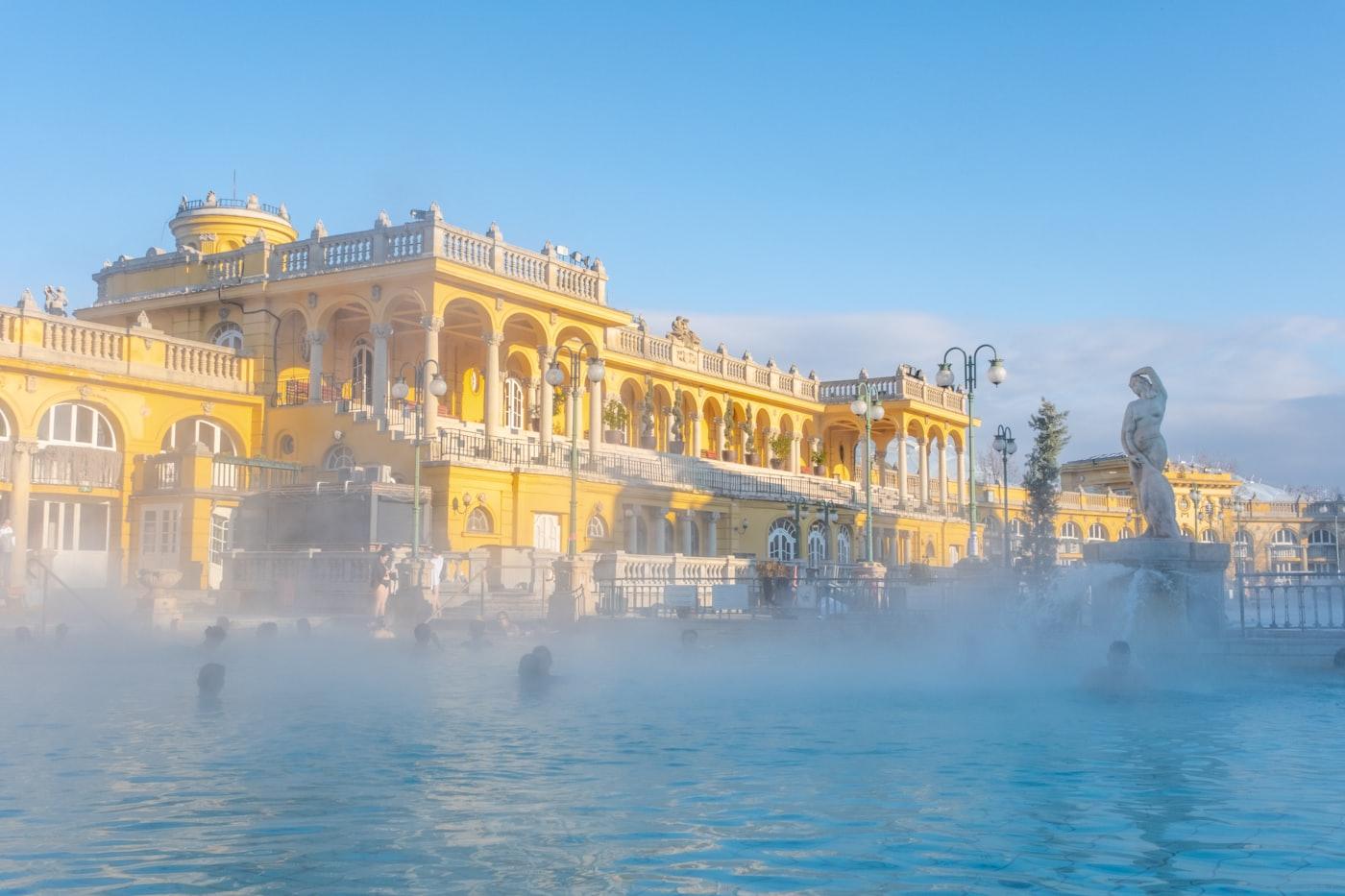 Dampf über dem Thermalbecken des Széchenyi-Bads in Budapest, dahinter der gelbe neobarocke Palast.